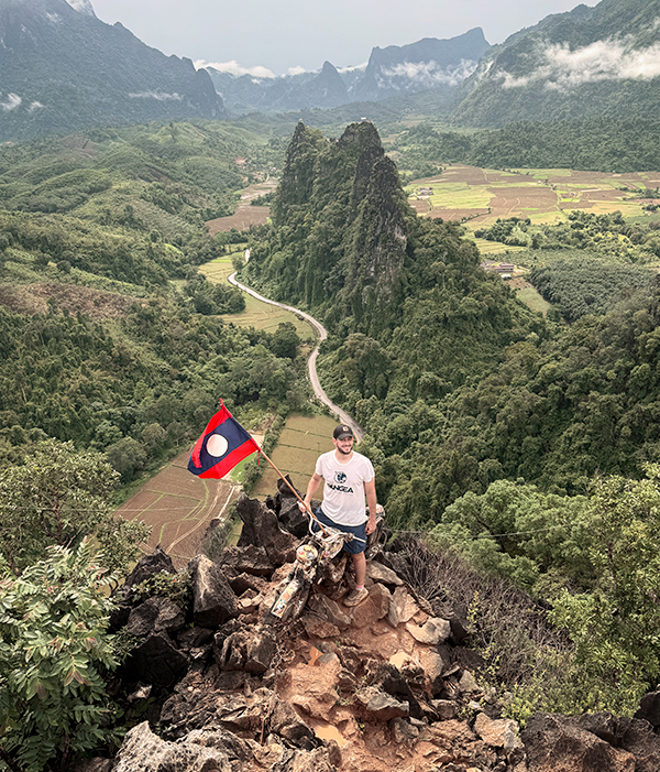 Imagen de una asesor experto de PANGEA en el en lo alto de una montaña en Laos ondeando la bandera con vistas panorámicas de fondo